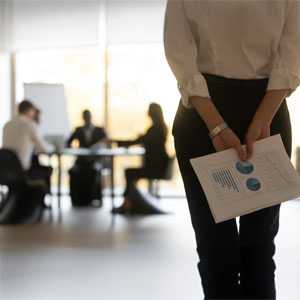 Businesswoman holding charts with blurred meeting in background.