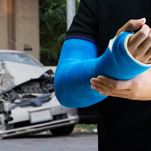 Person with a blue arm cast and a wrecked car, representing a minor injured in a summer job in Florida.